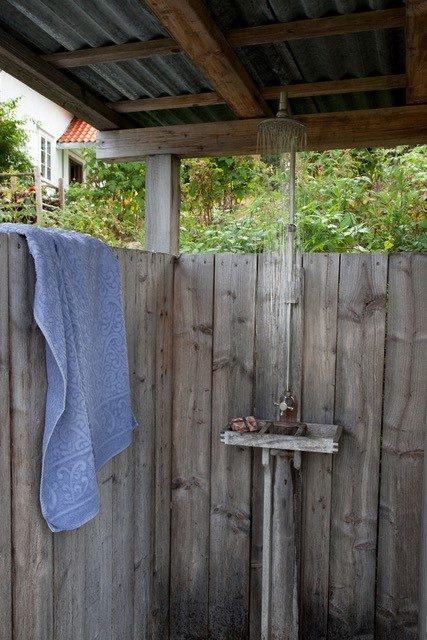Utedusj under tak, skjermet av en vegg av gråværet treverk med et håndkle over kanten