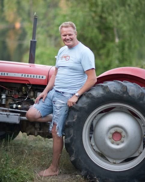 Lars smiler, barbent i shorts, lent mot det store bakhjulet på den gamle røde Massey Ferguson-traktoren